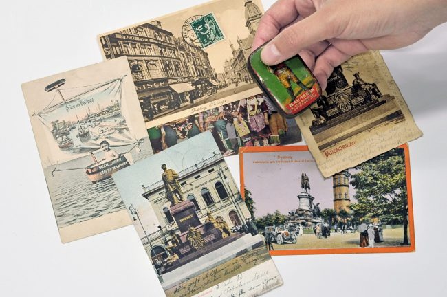 Verschiedene Postkarten mit Abbildungen des Bismarck-Denkmals in Duisburg. Außerdem eine historische Tabakdose der Firma Böninger mit rassistischem Werbemotiv.
