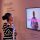 Eine junge Schwarze Frau hört sich ein Erklärvideo zum Thema "Kolonialismus" in der Ausstellung Überseehen an.