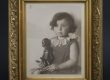 Kinderfoto von Inge Stern, ca. zwei-jähriges Mädchen sitzt mit ernstem Gesicht aufrecht, mit Schwarzer Puppe in der Hand; Schwarz-weiß-Fotografie in goldenem Rahmen; Inventarnummer 2020:0019; Sammlung ZfE, Kultur- und Stadthistorisches Museum Duisburg
